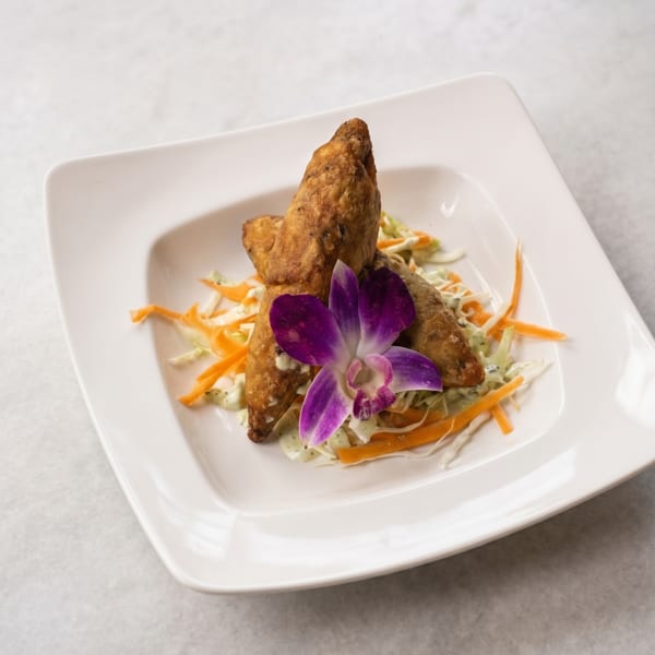 Crispy fried spring rolls on a bed of shredded cabbage and carrots, garnished with a purple orchid.