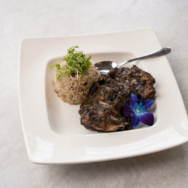 Jerk chicken with rice and peas, garnished with cilantro and a blue orchid, on a white plate.