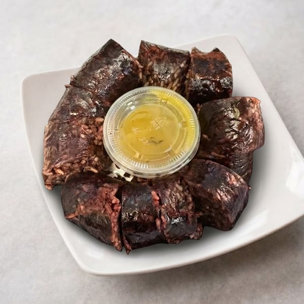 Sliced Korean blood sausage (sundae) with a small container of yellow dipping sauce on a white plate.