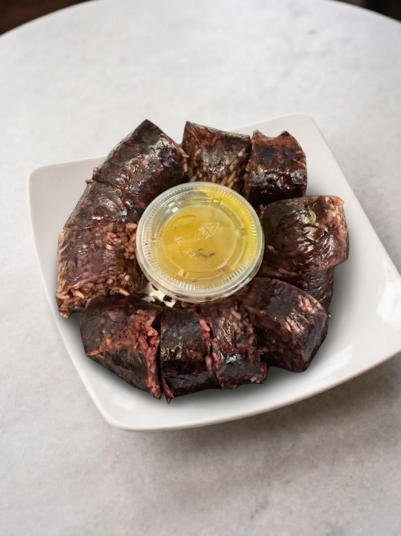 Sliced Korean blood sausage (sundae) with a small container of yellow dipping sauce on a white plate.