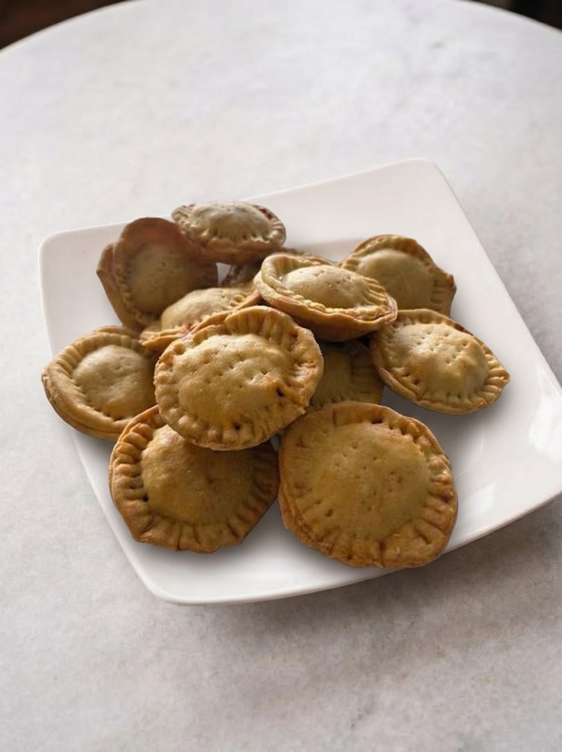 A white square plate filled with a pile of golden-brown, crimped mini empanadas on a light surface.