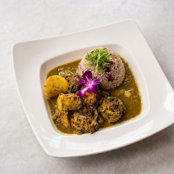 Curried chicken and potatoes in a green sauce, with rice and a purple orchid on a white plate.