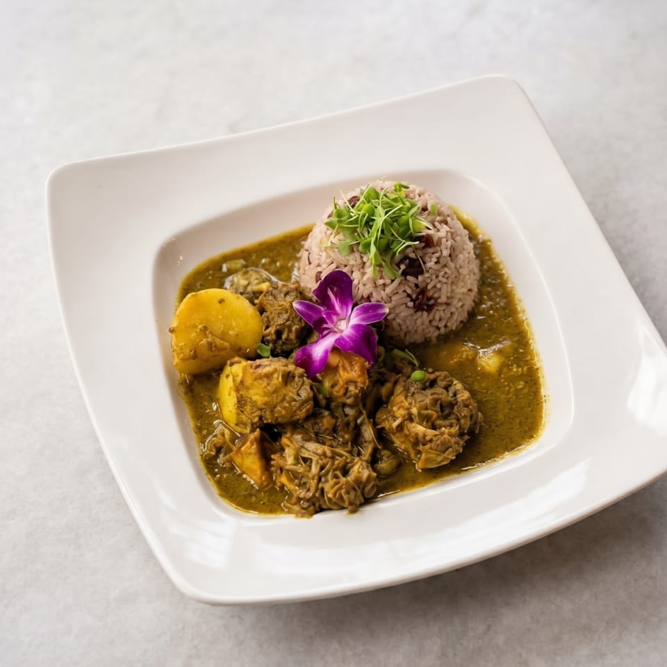Curried chicken and potatoes in a green sauce, with rice and a purple orchid on a white plate.